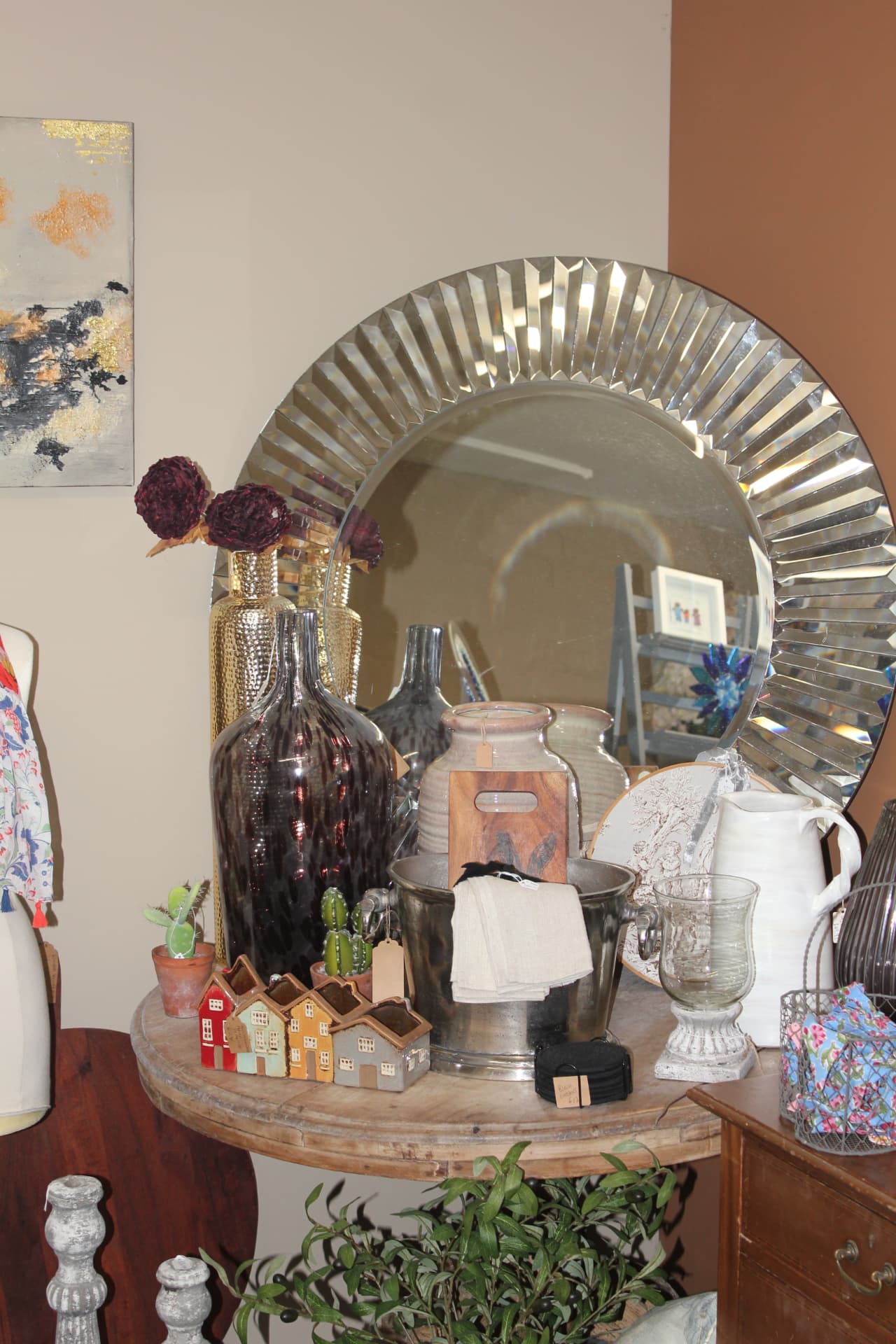 A round bevelled mirror above a table of glass and ceramics